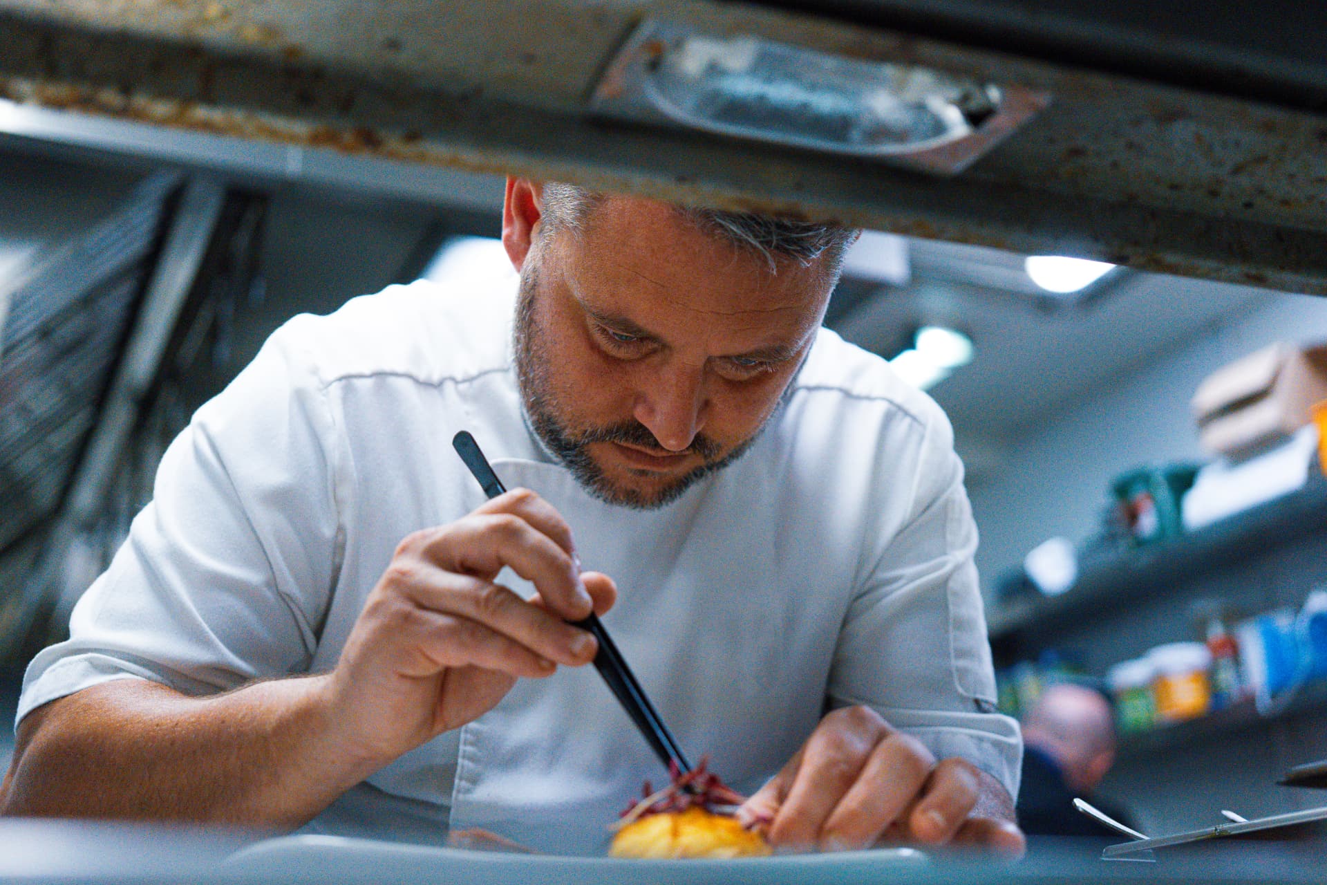 A chef finishing a plated dish with tweezers at the pass