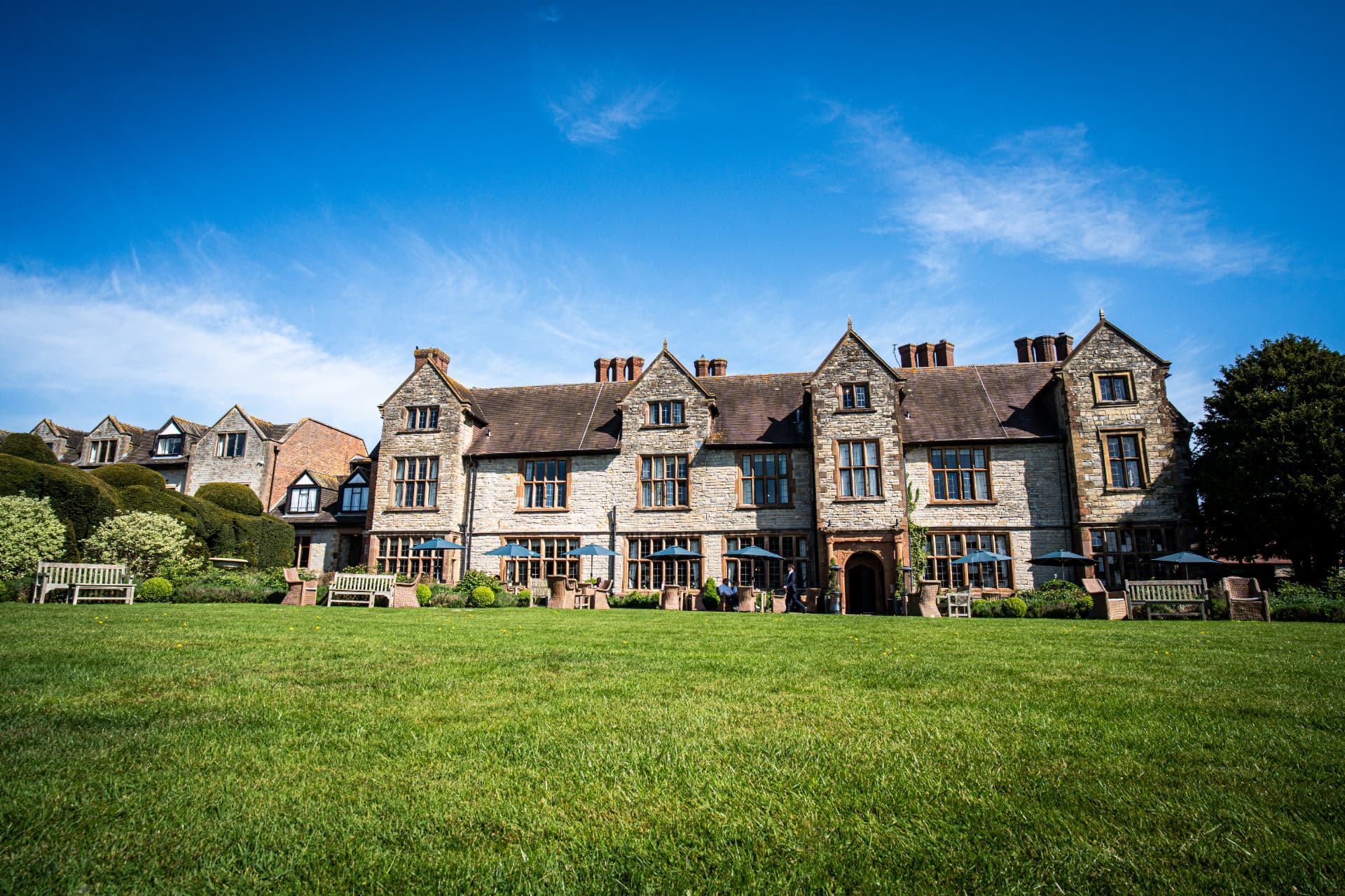 A stone country-house hotel beneath a bright blue sky, seen across a wide lawn
