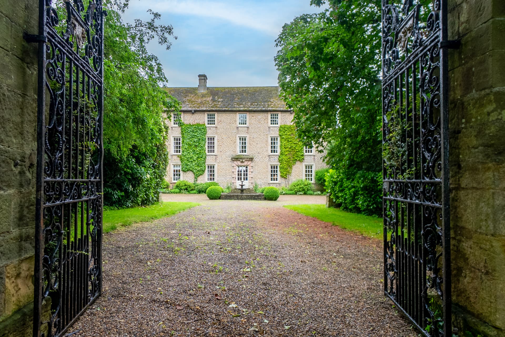 Wrought-iron gates opening onto the drive of a Georgian manor house